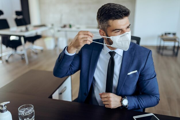 オフィスで働いている間保護フェイスマスクを身に着けているビジネスマン