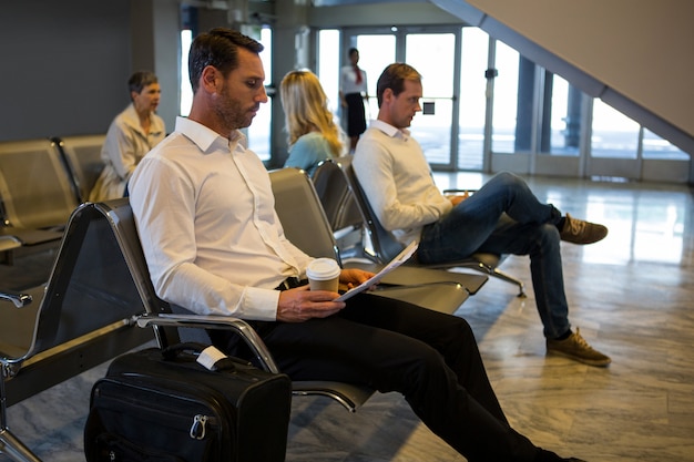 Free photo businessman reading newspaper in waiting area