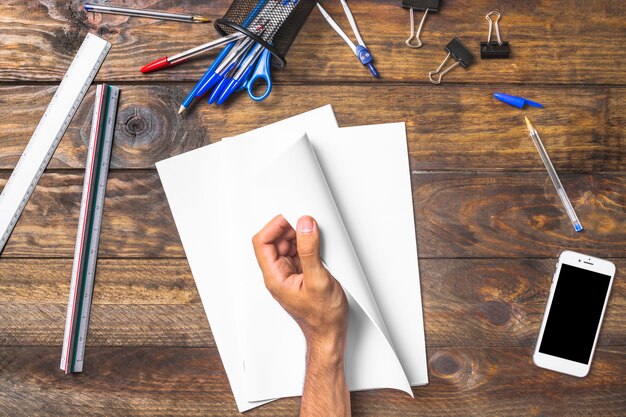 Businessman's hand holding white paper with stationeries and cellphone on table