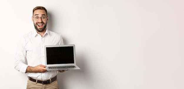 Foto gratuita uomo d'affari che mostra lo schermo del laptop che sembra eccitato in piedi su sfondo bianco