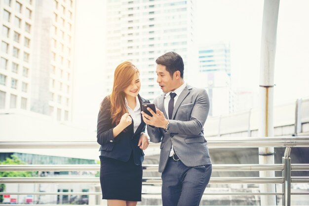 Businessman showing mobile phone to colleague outside.