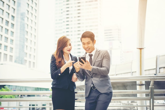 Businessman showing mobile phone to colleague outside.