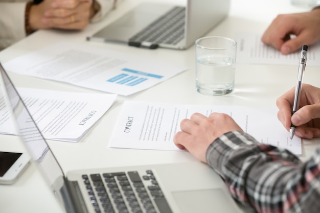 Businessman signing business contract filling document form at meeting, closeup