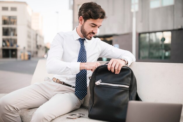 Businessman sitting on bench looking inside his backpack