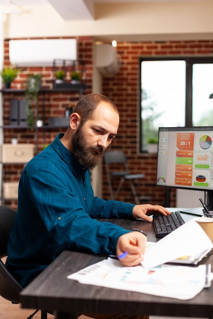 Foto gratuita uomo d'affari seduto alla scrivania che analizza i documenti aziendali che lavorano alla pianificazione della presentazione della gestione della strategia aziendale nell'ufficio di avvio. imprenditore guardando documenti di marketing