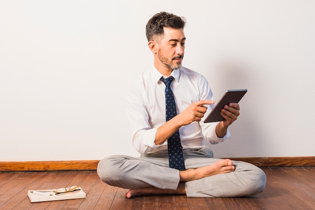 Бизнесмен, сидя на деревянный пол с помощью цифрового планшета