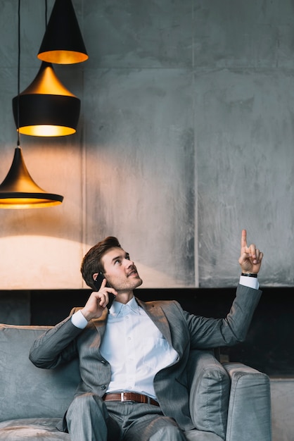 Free photo businessman sitting on sofa talking through cellphone looking up