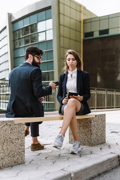 Businessman sitting with businesswoman looking at smartphone sitting on bench