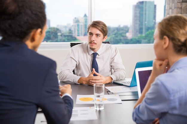 Free photo businessman sitting with a laptop talking to other colleagues