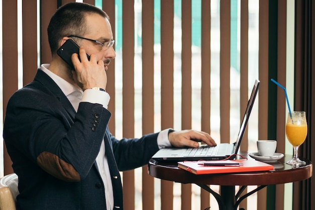 Free photo businessman speaking on hone and using laptop