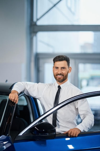 Businessman standing at auto salon and smiling on camera