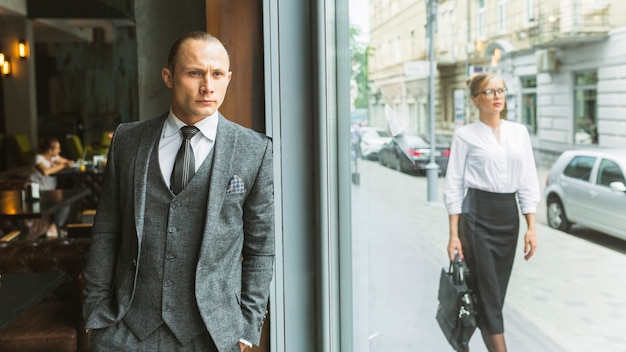 Businessman standing by cafe window near woman walking on sidewalk