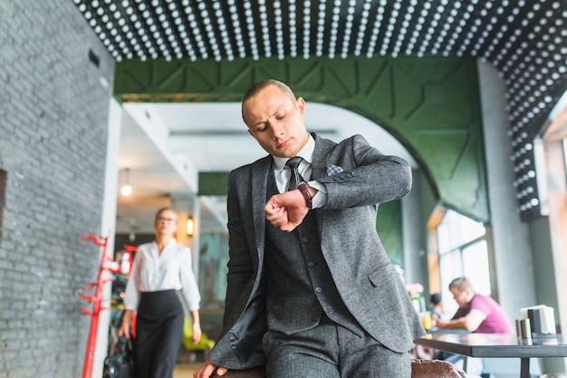 Foto gratuita uomo d'affari in vestito che controlla tempo sul suo orologio al ristorante