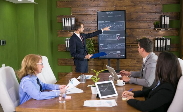 Businessman in suit having a presentation with charts on tv screen in the conference rom. Team meeting.