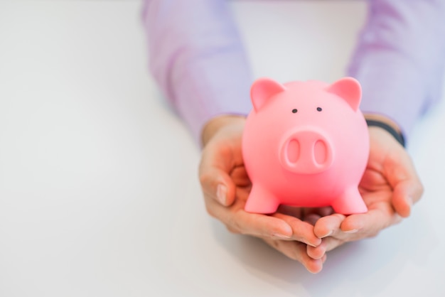 Businessman in a suit holding pink piggy bank with both hands, isolated on white background.