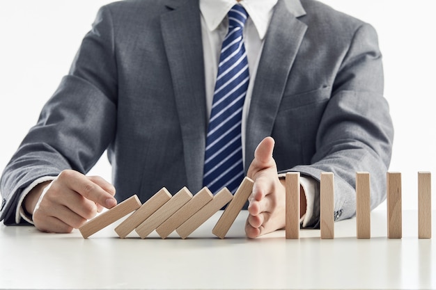 Free photo businessman in a suit protecting wooden blocks from falling in a domino effect