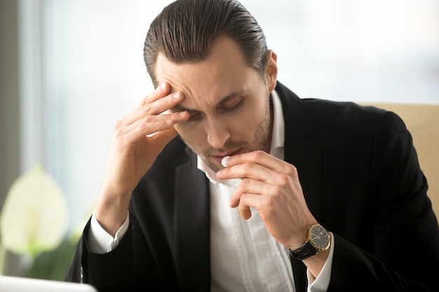 Бизнесмен принимает таблетки от головной боли в офисе