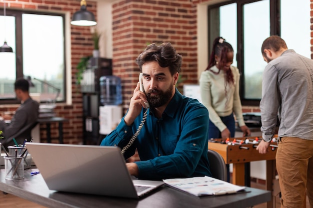 Businessman taking at phone with manager discussing company turnover while working at marketing strategy in startup office. Diverse businesspeople brainstorming ideas planning business collaboration