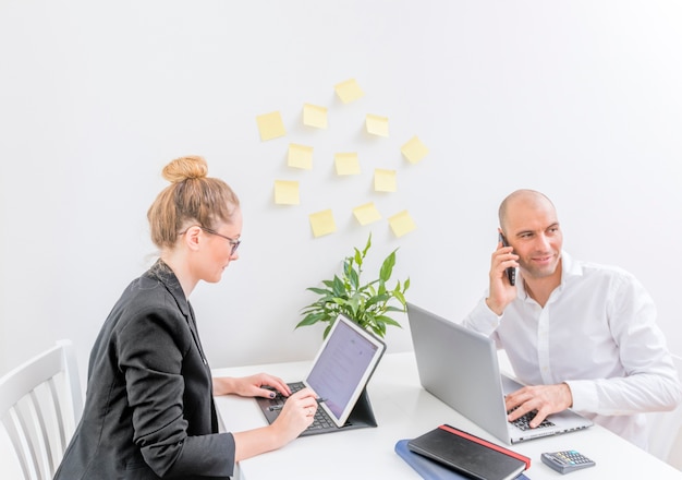 Businessman talking on cellphone while his partner working on laptop in office