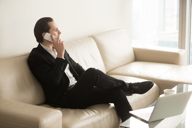 Businessman talks on the phone while sitting on couch.