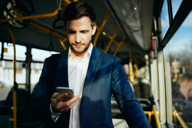 Businessman text messaging on mobile phone while traveling to work by public bus