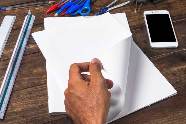 Businessman turning white blank paper with stationeries and smartphone on wooden table