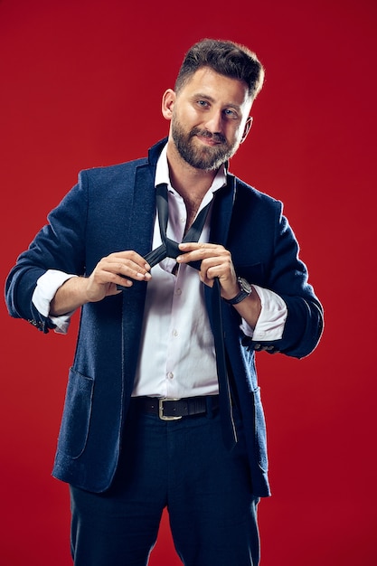 Businessman tying his tie at studio. Smiling business man standing isolated on red studio.