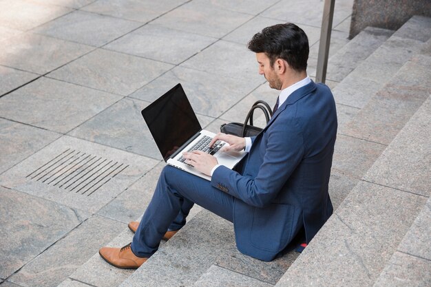Businessman typing on laptop on street