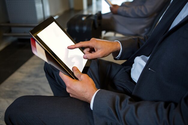 空港ターミナルに座っている間デジタルタブレットを使用するビジネスマン