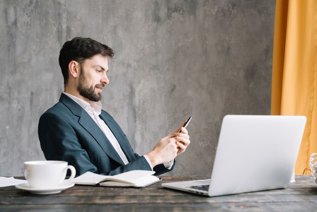 Businessman using smartphone near laptop