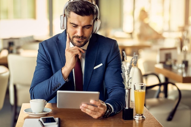 Businessman wearing headphones while surfing the net on touchpad in a cafe