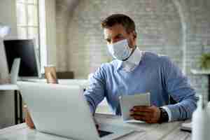 Free photo businessman wearing protective face mask while working on a computer and using digital tablet in the office