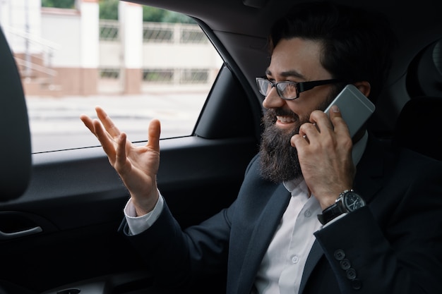A businessman while traveling by car in the back seat using a smartphone