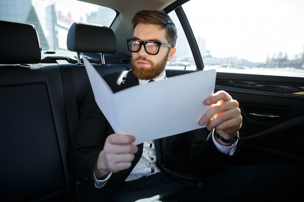 Uomo d'affari con i documenti che guidano sul sedile posteriore dell'automobile