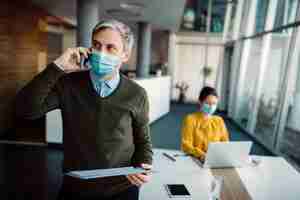 Free photo businessman with face mask making a phone call while analyzing reports in the office