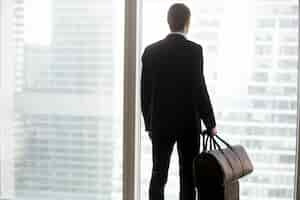 Free photo businessman with luggage standing in front of large window.