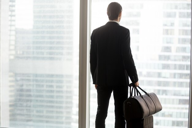 Бизнесмен с багажом, стоя перед большим окном.