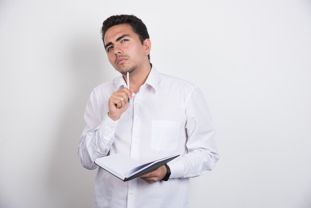 Businessman with notebook thinking hard on white background.