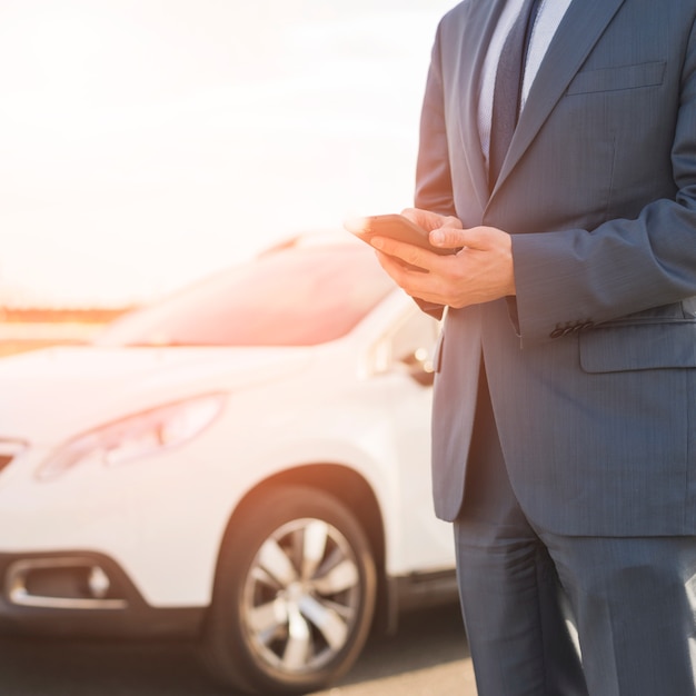 Businessman with smartphone in front of car