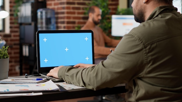 Businessman working on freelance with greenscreen on laptop in company office. Looking at pc display with blank chroma key template and isolated copyspace mockup on background.