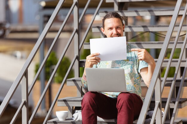 Businessman working outdoors with laptop, holding blank paper