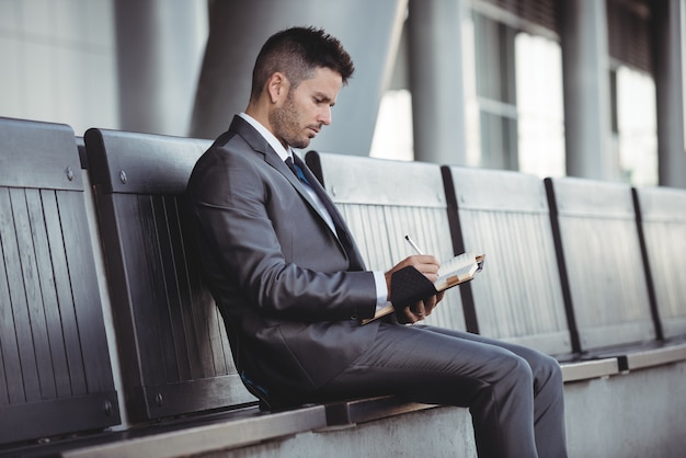 Businessman writing in his diary while sitting on a bench