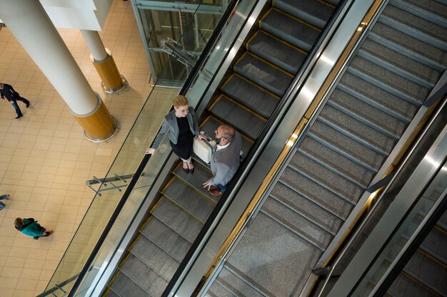 Businesspeople interacting with each other while moving down on escalator