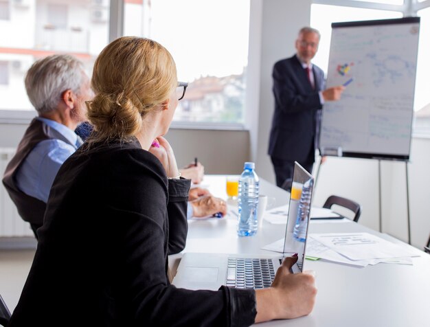 Businesspeople looking at man giving presentation on flip chart