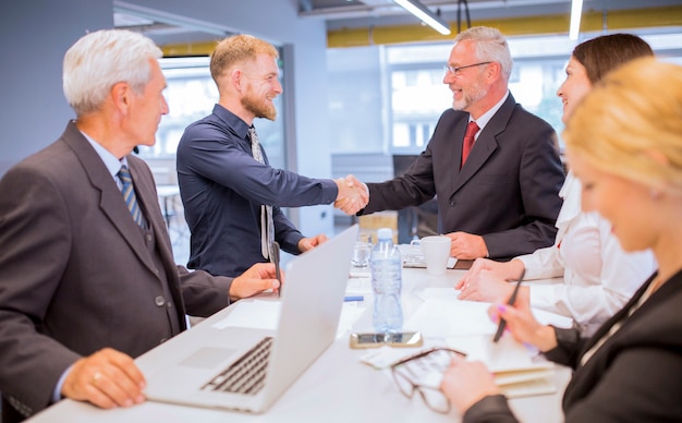 Businesspeople looking at two businessmen shaking hands in the business meeting