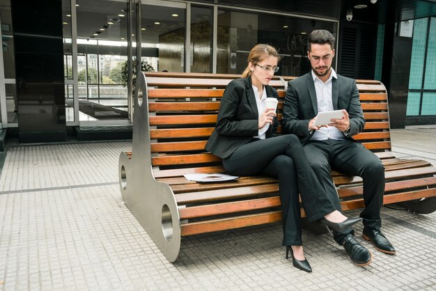 Businesspeople sitting on bench looking at mobile phone