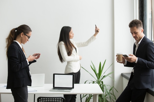 Бизнесмены с помощью смартфонов текстовых сообщений, принимая селфи в офисе во время перерыва