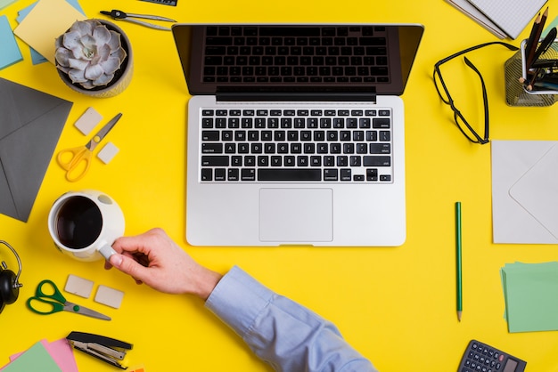 Businessperson holding cup of coffee and laptop over the yellow background