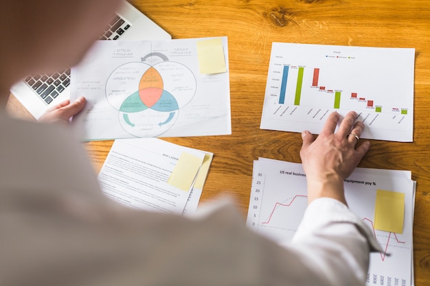 Free photo businessperson's hand analyzing graph over wooden desk