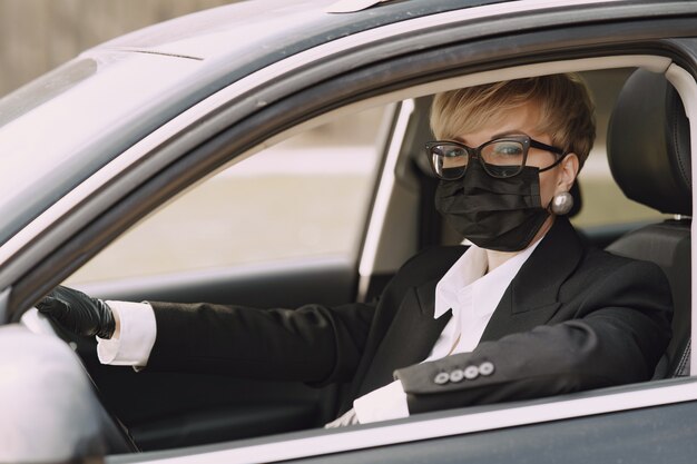 Деловая женщина в черной маске сидит в машине